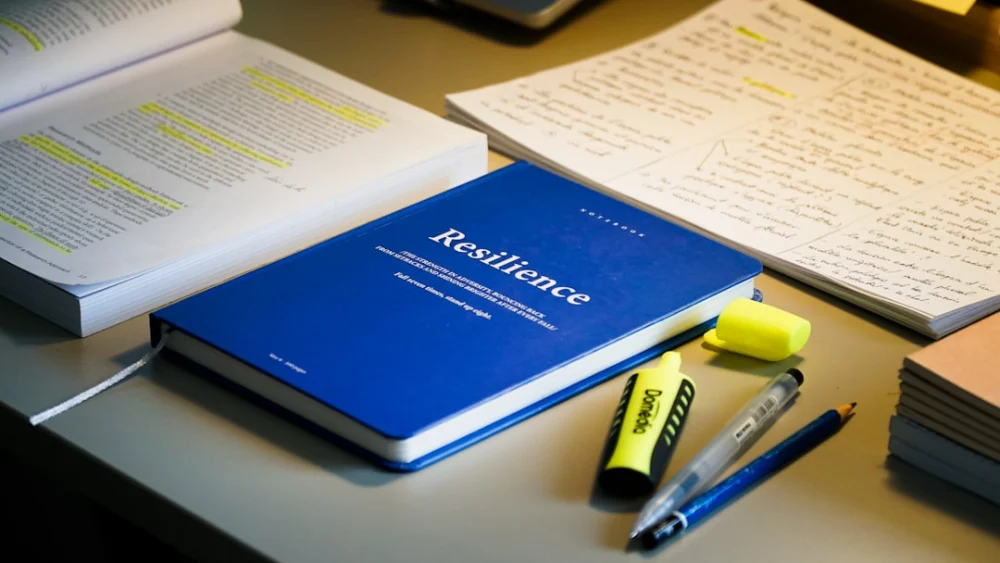 Blue book titled resilience with study materials and pens