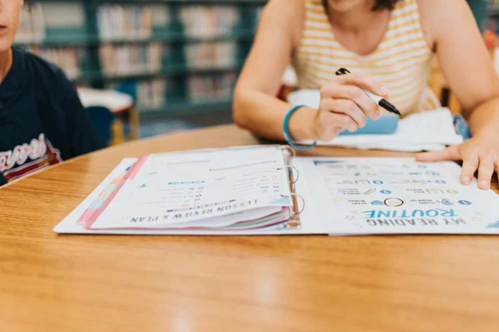 Student writing in an open binder on a wooden table