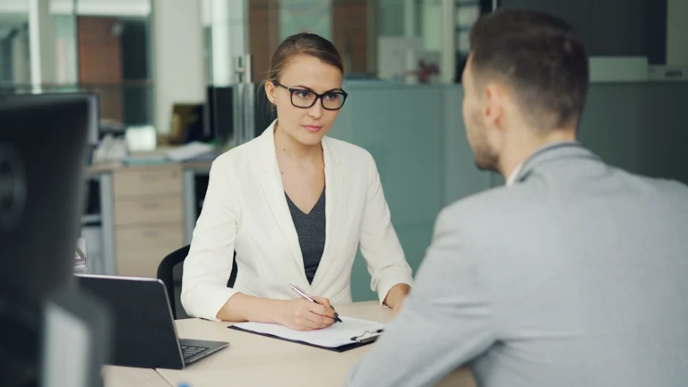 Woman in glasses interviews man at office desk