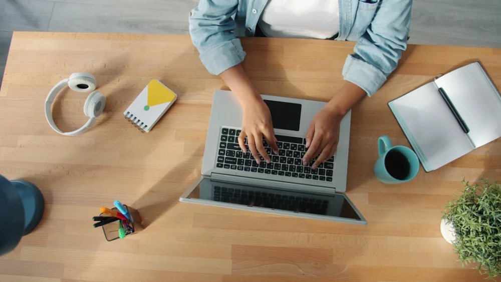 Person typing on a laptop at a wooden desk