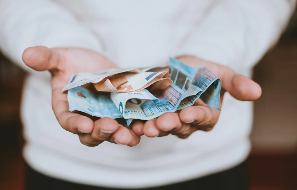 A person holding a handful of crumpled euro banknotes in their cupped hands