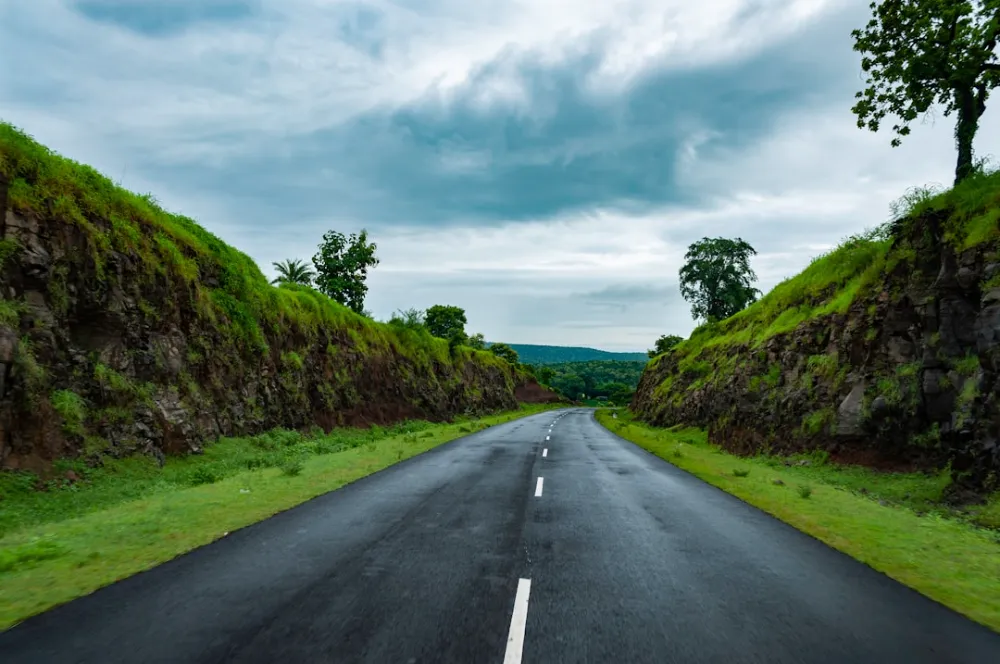 gray concrete road between green grass field under white clouds during daytime