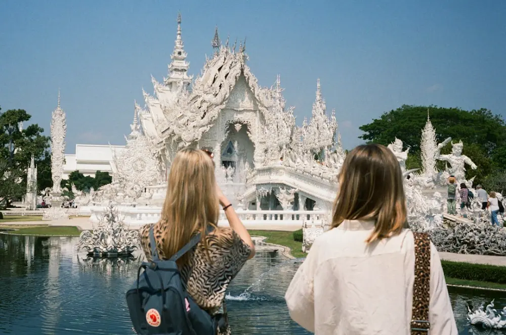 Two women admire a white ornate temple with water