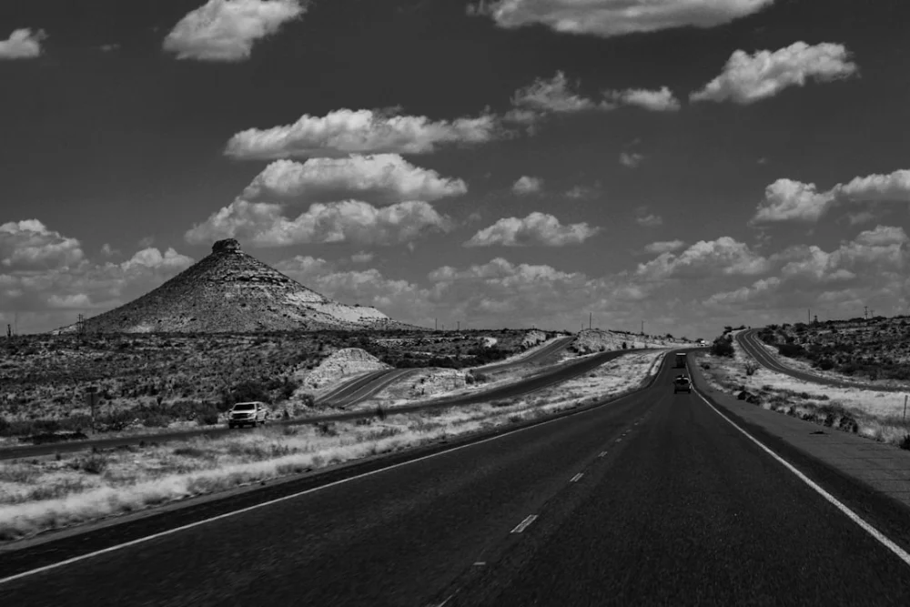 a black and white photo of a road with a mountain in the background