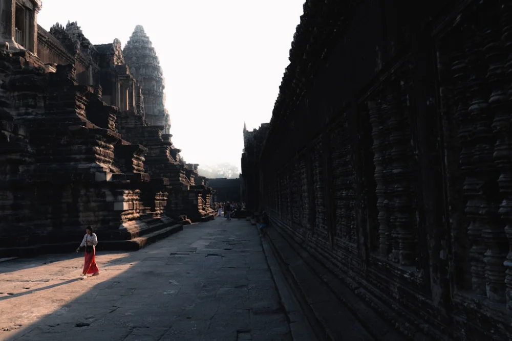 A person in a red skirt walks at angkor wat