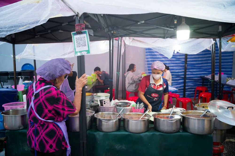 People working at a food stall with many pots