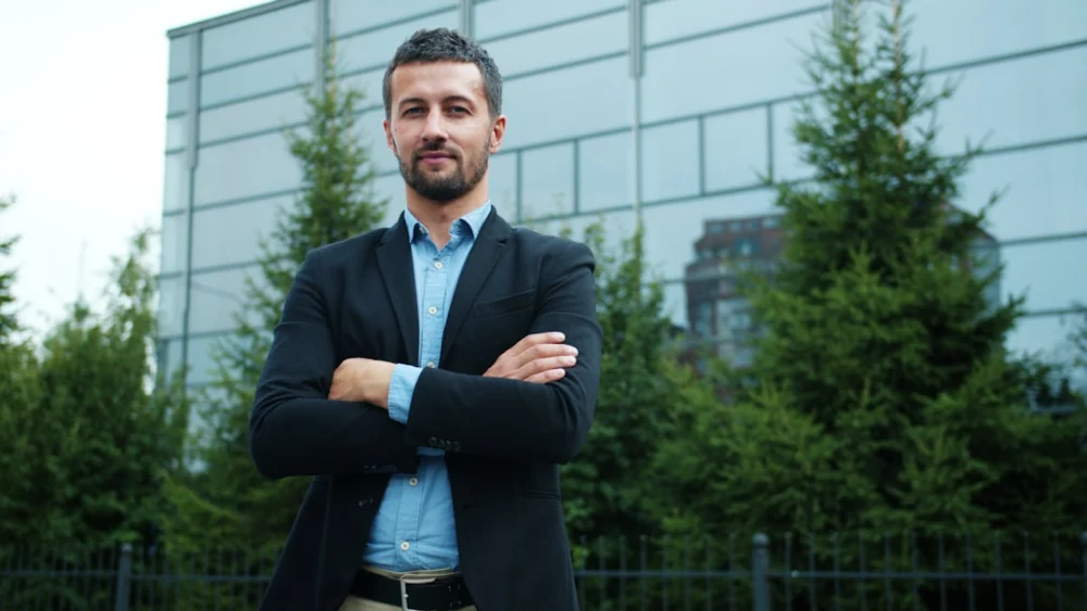 Man in suit standing with arms crossed outdoors