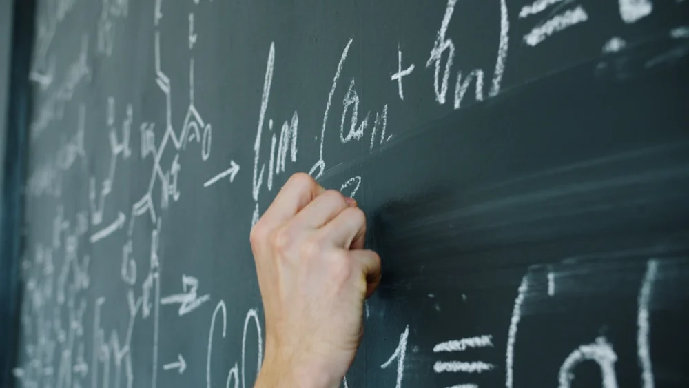 Hand writing mathematical formulas on a blackboard with chalk