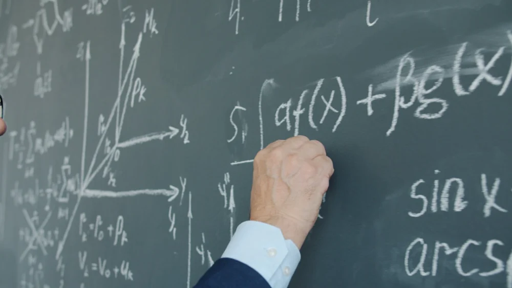 Teacher writing mathematical formulas on a blackboard