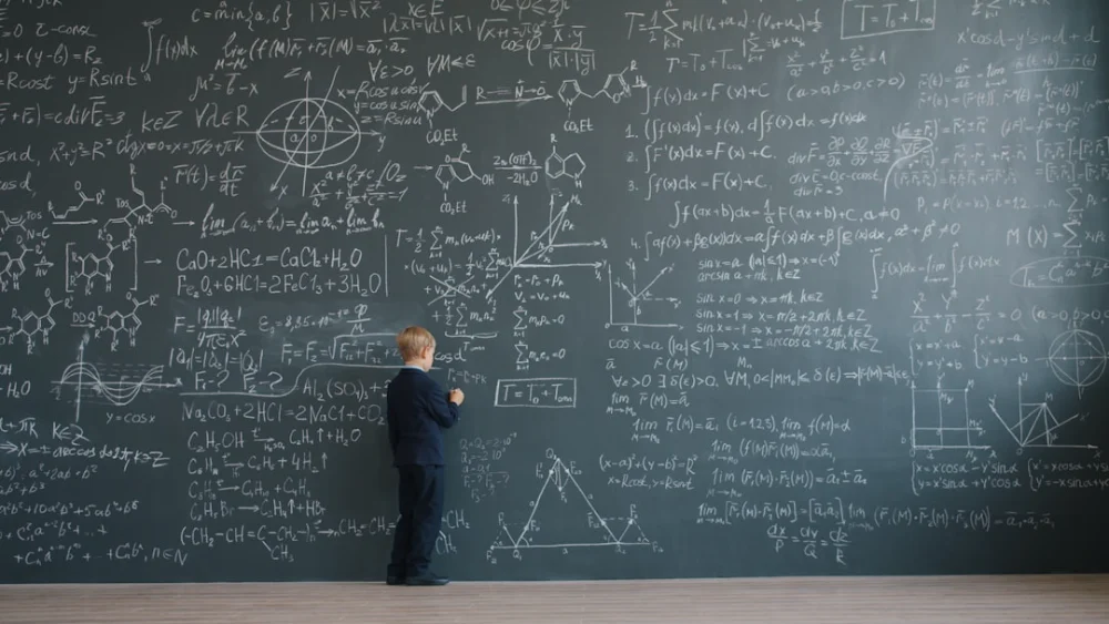 Boy standing before a blackboard covered in equations