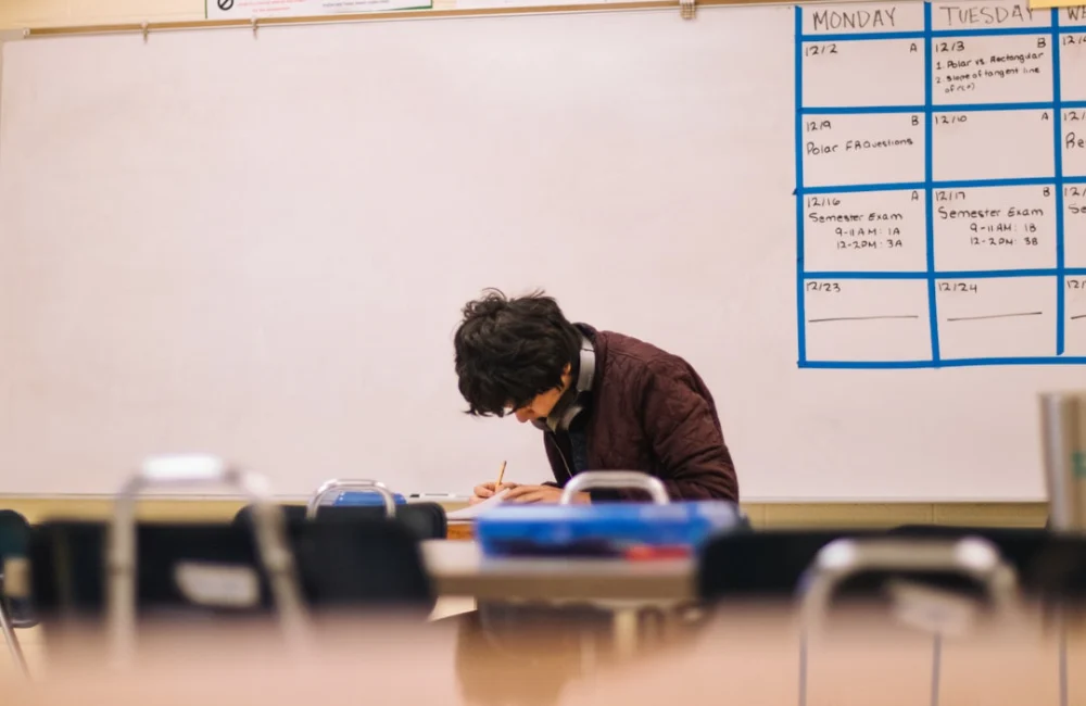 A student writing on paper at a desk in a classroom