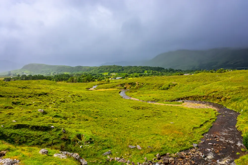 A winding stream flows through a vast green field