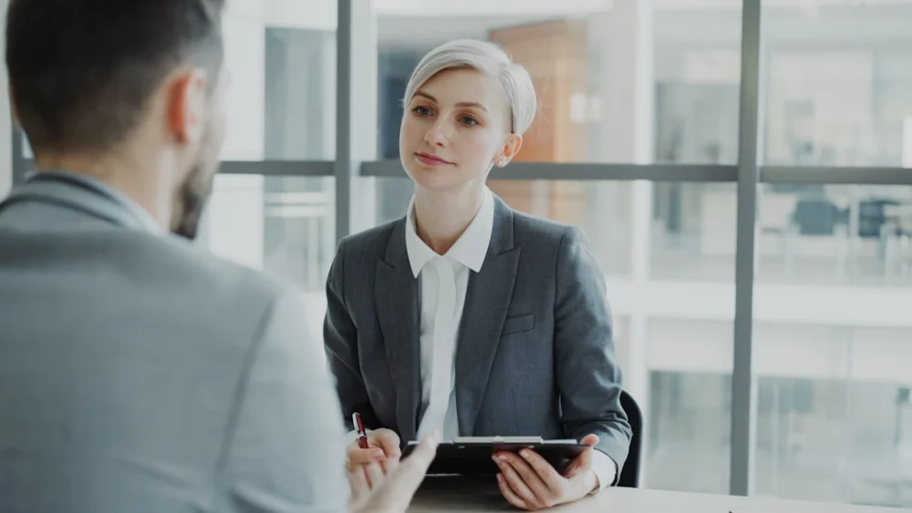 Woman in suit interviews man at desk