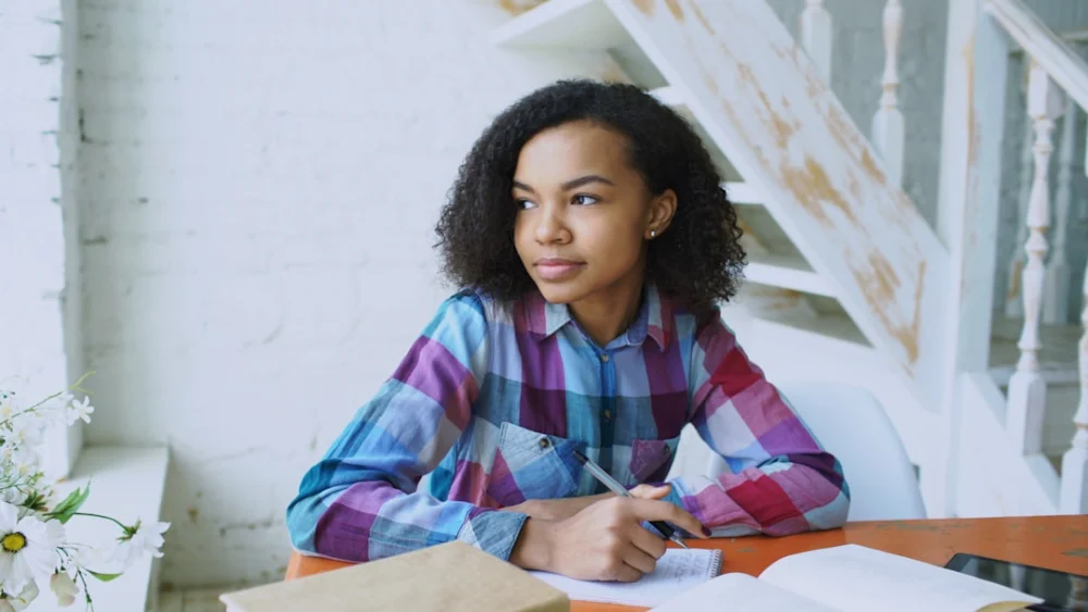 Young woman writing at a table with open book