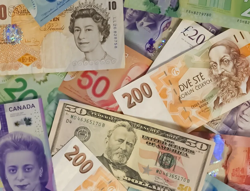 A collection of international banknotes including US dollars, British pounds, and Czech koruna