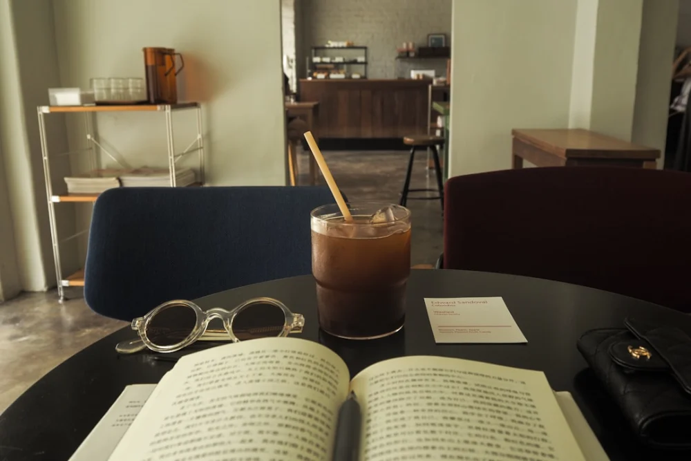 Open book, iced coffee, and glasses on a cafe table