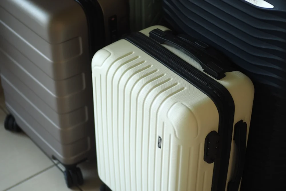 Three hard-shell suitcases in white, grey, and dark colors