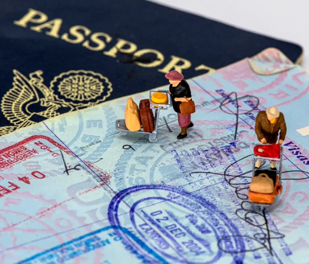 Two miniature figures with luggage carts on a passport page with travel stamps