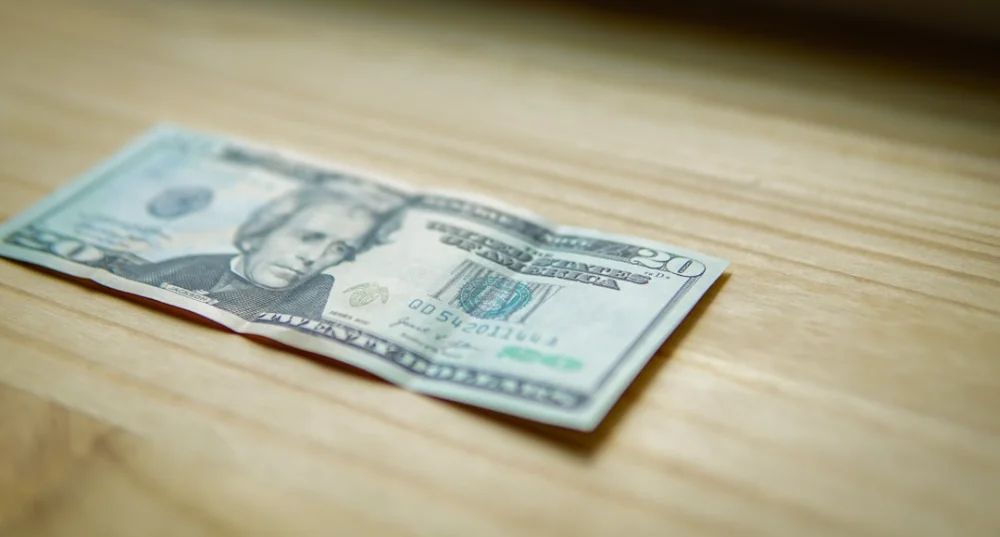 A twenty-dollar bill lies on a wooden table