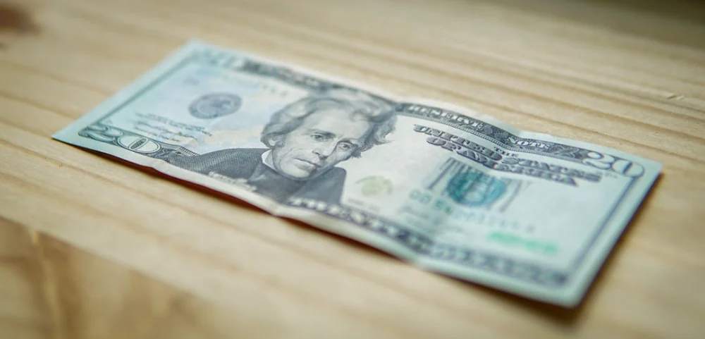 A crumpled twenty-dollar bill on a wooden surface