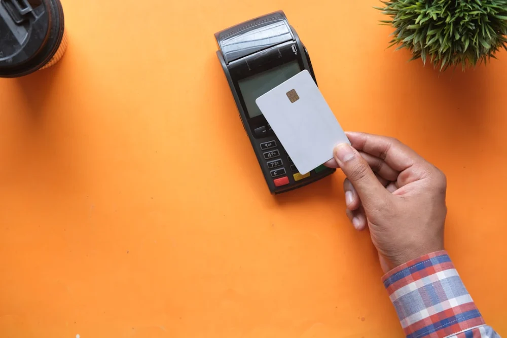 A person holding a blank credit card near a payment terminal on orange